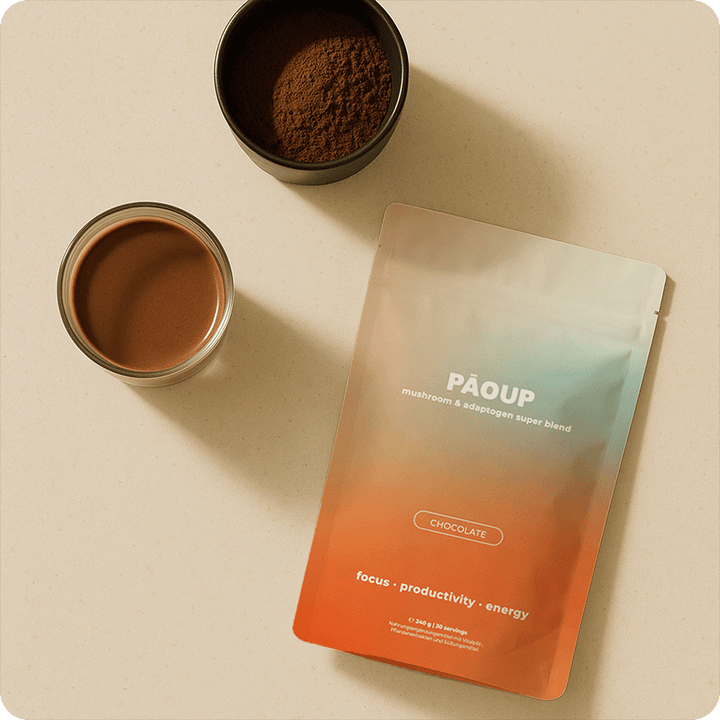 PAOPUP chocolate powder package with a cup of coffee and a bowl of ground coffee on a beige surface